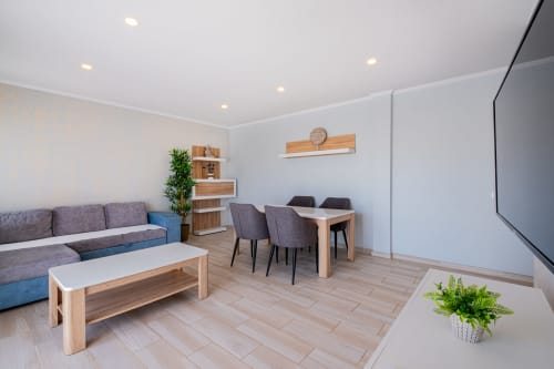 Sala de estar moderna do Signature Stays com sofá cinzento, móveis em madeira, mesa de jantar e plantas em vaso