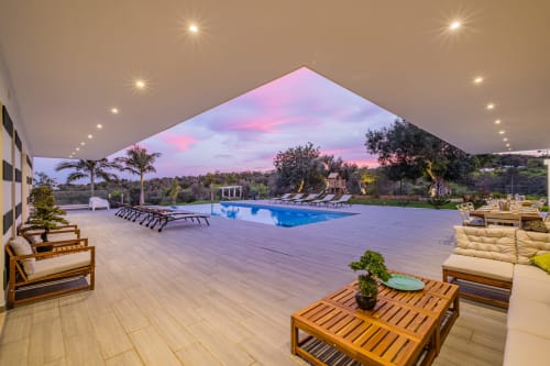 Terraço de piscina de luxo na Signature Stays Portugal com espreguiçadeiras, piscina azul e vistas do pôr do sol sobre a paisagem
