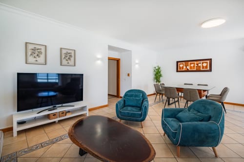 Sala de estar moderna no Signature Stays com poltronas verde-azulado, TV, área de refeições e decoração contemporânea