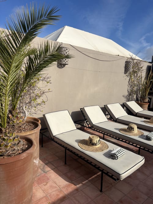 Transats sur la terrasse avec chapeaux de paille au Riad 191 à Marrakech, ombragés par un auvent blanc et des palmiers