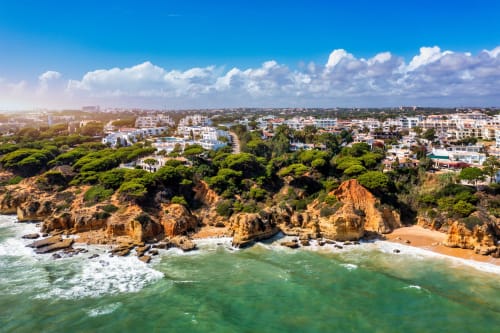 Resort à beira do penhasco com formações rochosas douradas, praia arenosa, oceano turquesa e edifícios brancos entre a vegetação
