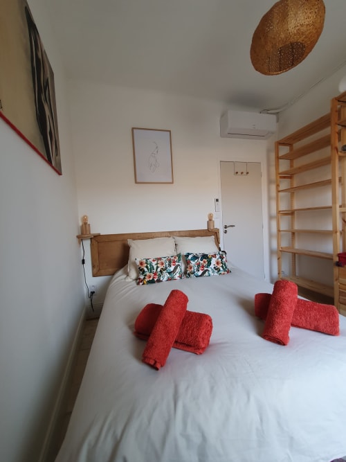 Chambre lumineuse du Mas des Ecoliers avec lit en bois, coussins colorés et lampe suspendue tressée en Provence