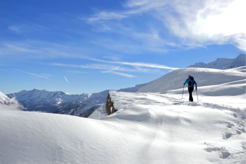 Sciatore su cresta alpina innevata vicino a Locana, Italia con vette montane e cielo azzurro limpido