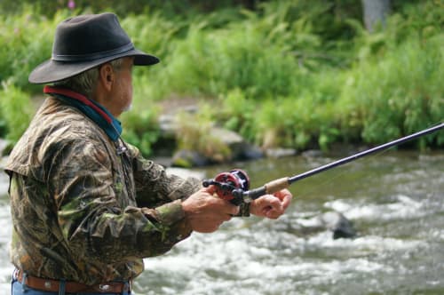 Uomo anziano a pesca con la mosca in un torrente di montagna nel rifugio di campagna di Locana, Italia