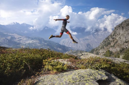 Corridore su trail che salta il terreno alpino vicino a Locana con picchi montani e valli sullo sfondo