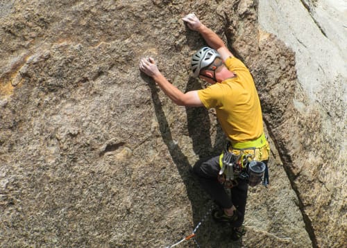 Arrampicatore in maglietta gialla scala parete di granito presso Locana, Italia meta avventura