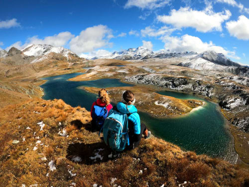 Due escursionisti con zaini che ammiranolaghi alpini e montagne innevate vicino a Locana, Italia