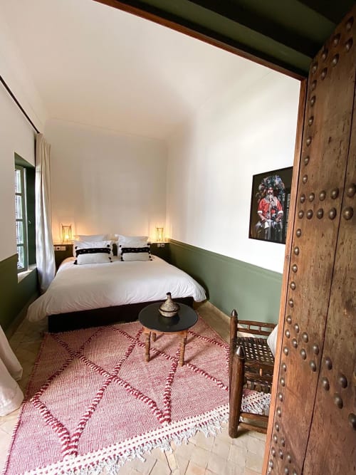 Chambre du Riad 191 Marrakech avec lit blanc, boiseries vertes, tapis géométrique rouge et porte en bois