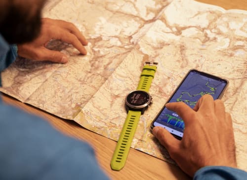 Ospite che pianifica un percorso escursionistico a Camere d'Aria a Locana usando una carta topografica, smartwatch e app GPS sullo smartphone