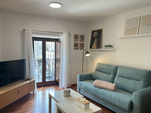Salón moderno en apartamento de Pontevedra con sofá verde, televisor y vistas al río a través de puertas acristaladas