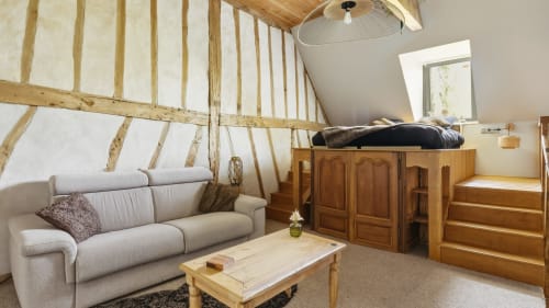 Chambre loft duplex avec poutres en bois, canapé gris, lit surélevé et ventilateur de plafond à L'Etoile De Forges BnB