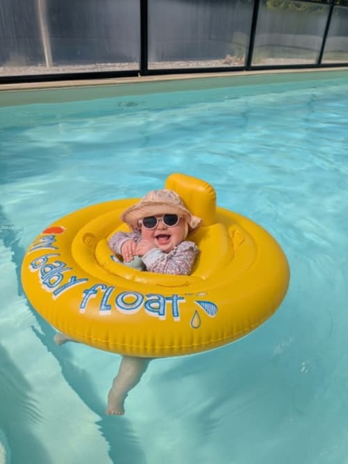 Petit enfant souriante dans une bouée jaune, piscine intérieure turquoise du Gîte de Ker Huon, Runan