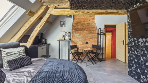 Studio loft moderne avec cheminée en briques apparentes, poutres en bois, lit double, coin repas et décoration thématique cinéma