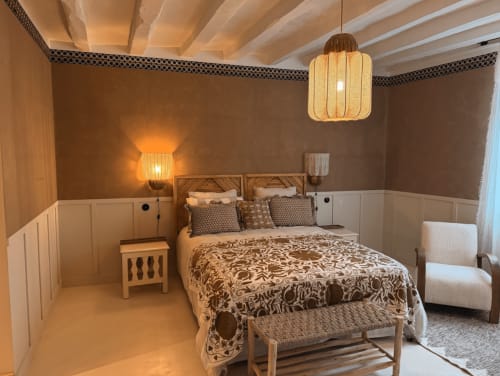 Chambre 'Ambre Brun' de la Maison Romy : murs marron chaud, poutres bois, luminaires suspendus et vue sur la ville