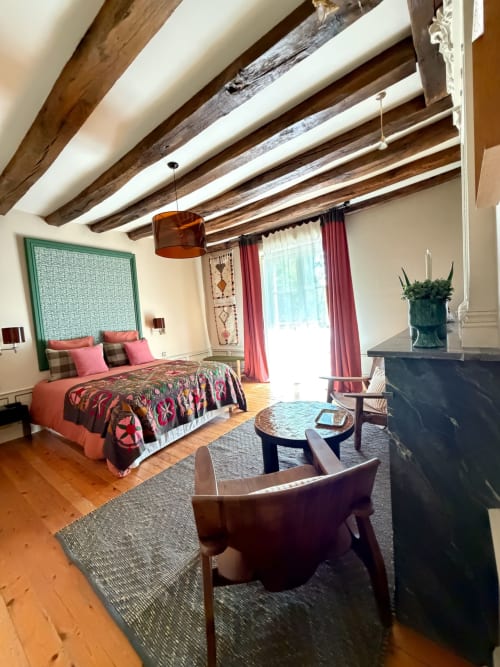 Chambre Maison Romy avec poutres apparentes, literie corail, tête de lit verte et coin salon moderne avec vue sur la ville