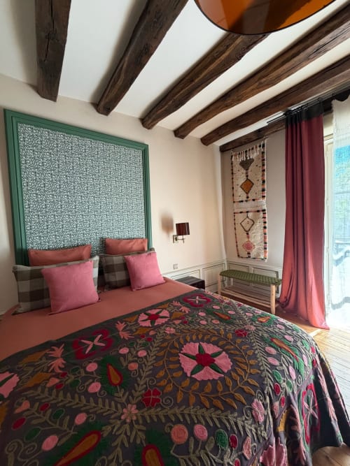 Chambre de la Maison Romy B&B avec poutres apparentes, literie fleurie ornée, accents roses et vue sur la ville