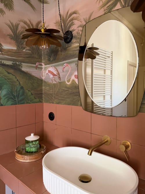 Salle de bain luxueuse à la Maison Romy avec carrelage corail, miroir ovale, robinetterie dorée et fresque tropicale