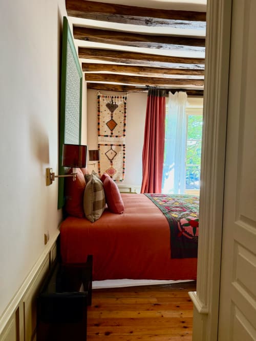 Chambre cosy de la Maison Romy B&B avec lit rouge, poutres apparentes, art mural tissé et vue sur la ville