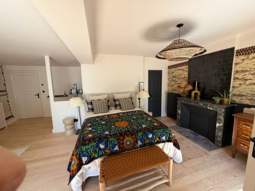 Chambre Balthazar de la boutique hôtel Maison Romy avec literie aux motifs colorés, cheminée noire, luminaire suspendu tressé et