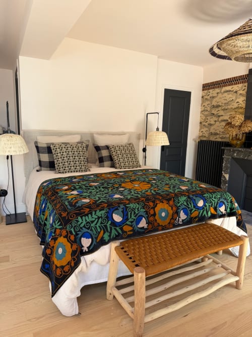 Chambre élégante à la Maison Romy avec couvre-lit floral coloré, suspensions en osier et banc en bois dans la suite Balthazar