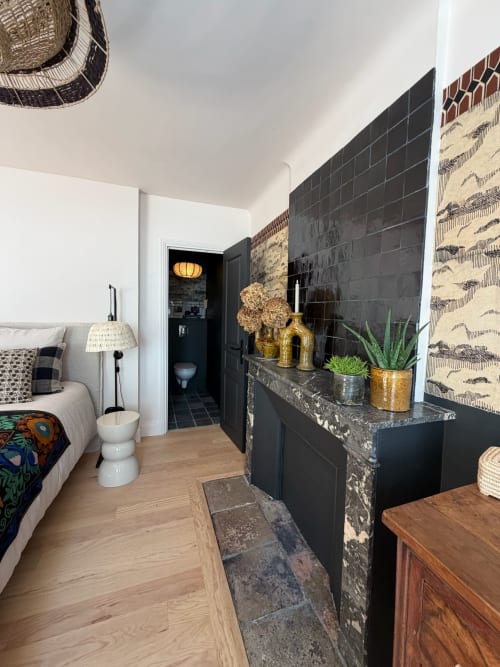 Chambre Balthazar à la Maison Romy avec cheminée en carrelage noir, décor doré, luminaire suspendu tressé et parquet vue ville