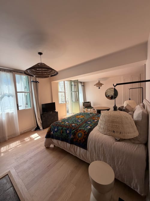 Chambre Balthazar à la Maison Romy B&B avec lits jumeaux, luminaire suspendu tressé, couverture colorée et vue sur la ville depuis le balcon