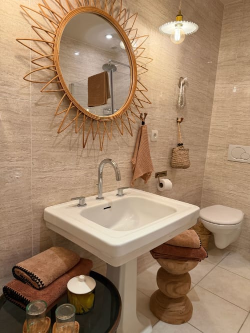 Salle de bain moderne à la Maison Romy avec miroir soleil, lavabo sur colonne et tons chauds terre dans ce gîte français