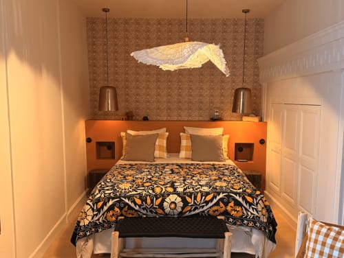 Chambre chaleureuse à la Maison Romy B&B avec tête de lit orange, luminaire poisson décoratif et literie floral donnant sur le jardin