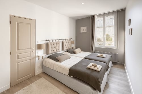 Chambre moderne lumineuse avec lits jumeaux, tête de lit beige, grandes fenêtres avec vue sur le jardin à l'hôtel Maunoury Citybreak à Chartres