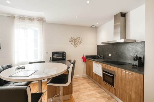 Cuisine moderne et coin repas de l'appartement à Chartres avec armoires en bois, plan de travail sombre et table ronde