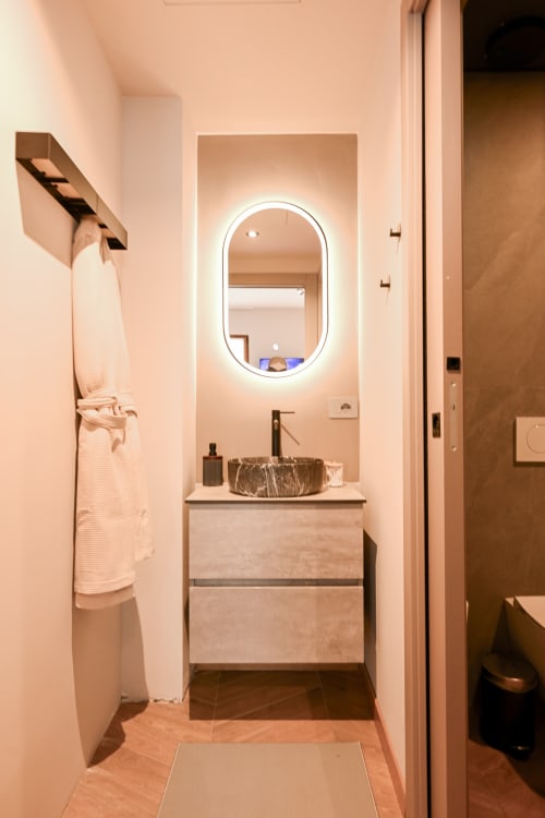 Bagno moderno a Casa Giulietta Como con specchio ovale illuminato, lavabo in pietra e mobile in legno