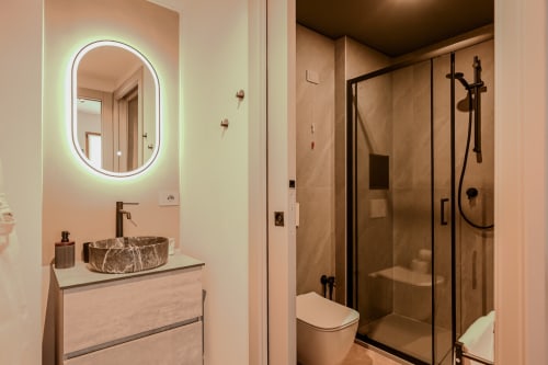 Bagno moderno presso Casa Giulietta Como con specchio LED ovale, lavabo in marmo e doccia con pavimento rialzato con finiture nere