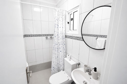 Banheiro moderno com azulejos brancos, borda decorativa, cuba de cerâmica, vaso sanitário e espelho circular na villa SpecialStays