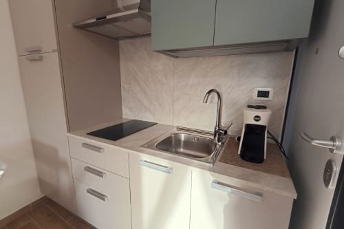 Moderna piccola cucina con armadiatura bianca, rivestimento in marmo, piano cottura a induzione e lavello in acciaio inossidabile a The Gentle Home
