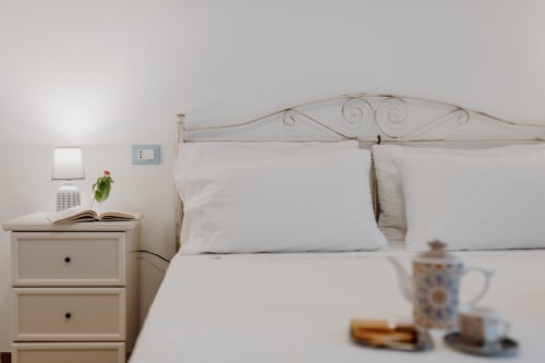 Camera luminosa con biancheria bianca, testata letto in ferro battuto e vista sul mare presso l'appartamento vacanze Il Porticcio a Villanova, Italia