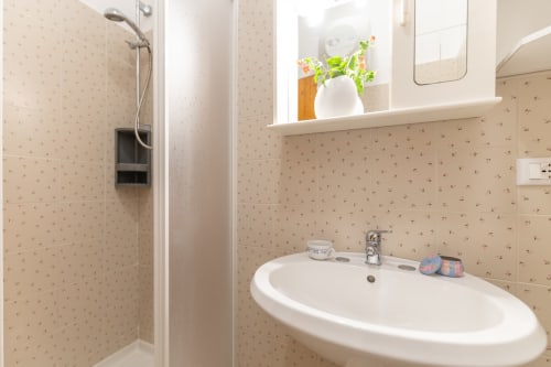 Moderno bagno con piastrelle beige, lavabo bianco ovale, zona doccia e specchio nell'appartamento Il Porticicolo, Villanova