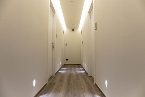 Corridoio moderno dell'hotel con pareti bianche, pavimenti in legno e luci LED al soffitto presso Mas Collection a Bari