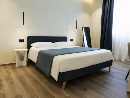 Modern double bedroom at Mas Collection hotel in Bari with black bed frame, white bedding, wooden flooring, and city view