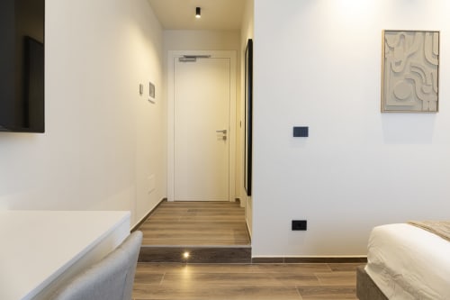 Ingresso moderno della camera d'hotel a Mas Collection Bari con pavimento in legno, porta bianca, letto e arte contemporanea