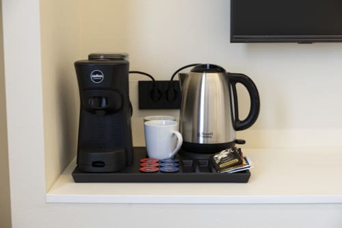 Stazione caffè nella camera dell'hotel Mas Collection con macchina Lavazza, bollitore Russell Hobbs, tazza bianca e capsule di tè sullo scaffale