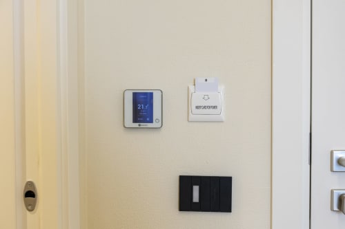 Parete beige con termostato digitale che mostra 21,7°C, lettore card chiave e interruttori della luce nella camera d'hotel Mas Collection, Bari