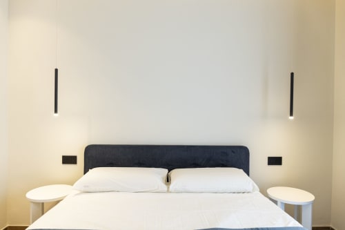 Camera moderna dell'hotel Mas Collection Bari con testata scura, cuscini bianchi, comodini rotondi e parete minimalista