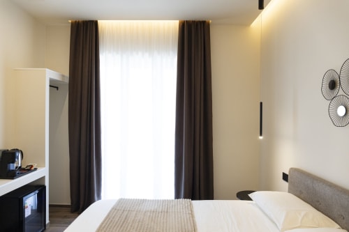 Camera moderna della Mas Collection Bari con letto matrimoniale, scrivania, tende marroni e vista città dal balcone