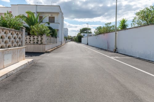 Edifici residenziali bianchi lungo una tranquilla strada a Villanova, Italia presso Il Porticciolo Vacanze con palme e cielo sereno