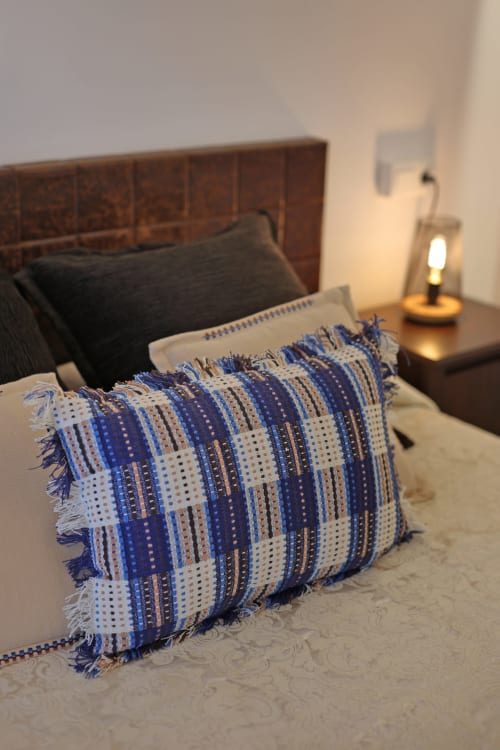 Almohada decorativa a rayas azules y blancas en la cama del hotel Torre de Quintana en Suances con lámpara de mesita de noche