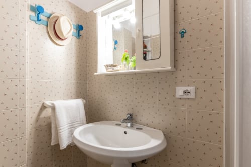 Bagno pulito con lavandino bianco rotondo, specchio e pareti rivestite in piastrelle beige decorative presso l'appartamento Il Porticciolo Vacanze