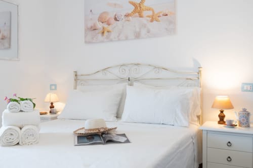 Camera da letto luminosa con biancheria bianca, stelle marine e conchiglie decorative, arredamento in stile costiero e vista sul mare presso Il Porticiolo