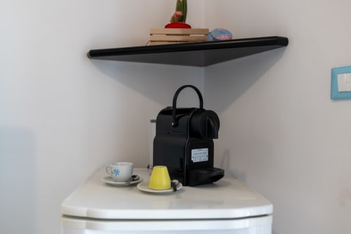 Mensola nera sopra il wc con macchina per il caffè, tazza, contenitore giallo per capsule e articoli decorativi nell'appartamento di Villanova