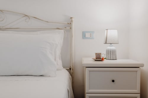 Camera da letto luminosa con letto in ferro battuto bianco, lampada sul comodino e arredamento minimalista a Il PorticcioloVacanze, Villanova
