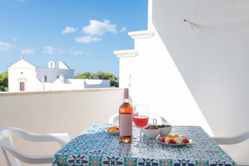 Terrazza mediterranea a Il Porticciolo con vino rosato, sedie bianche e vista della chiesa storica di Villanova
